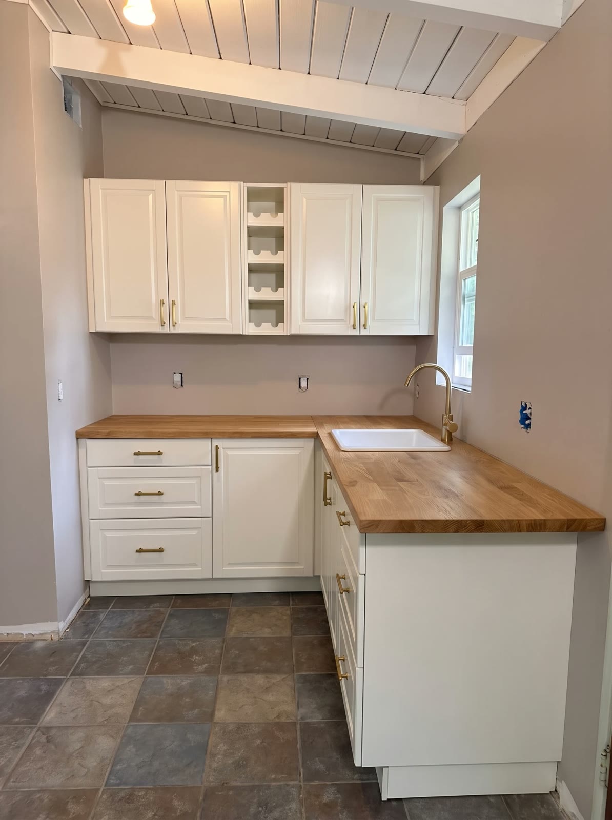 The kitchen after: white shaker cabinets, an oak counter and brass hardware